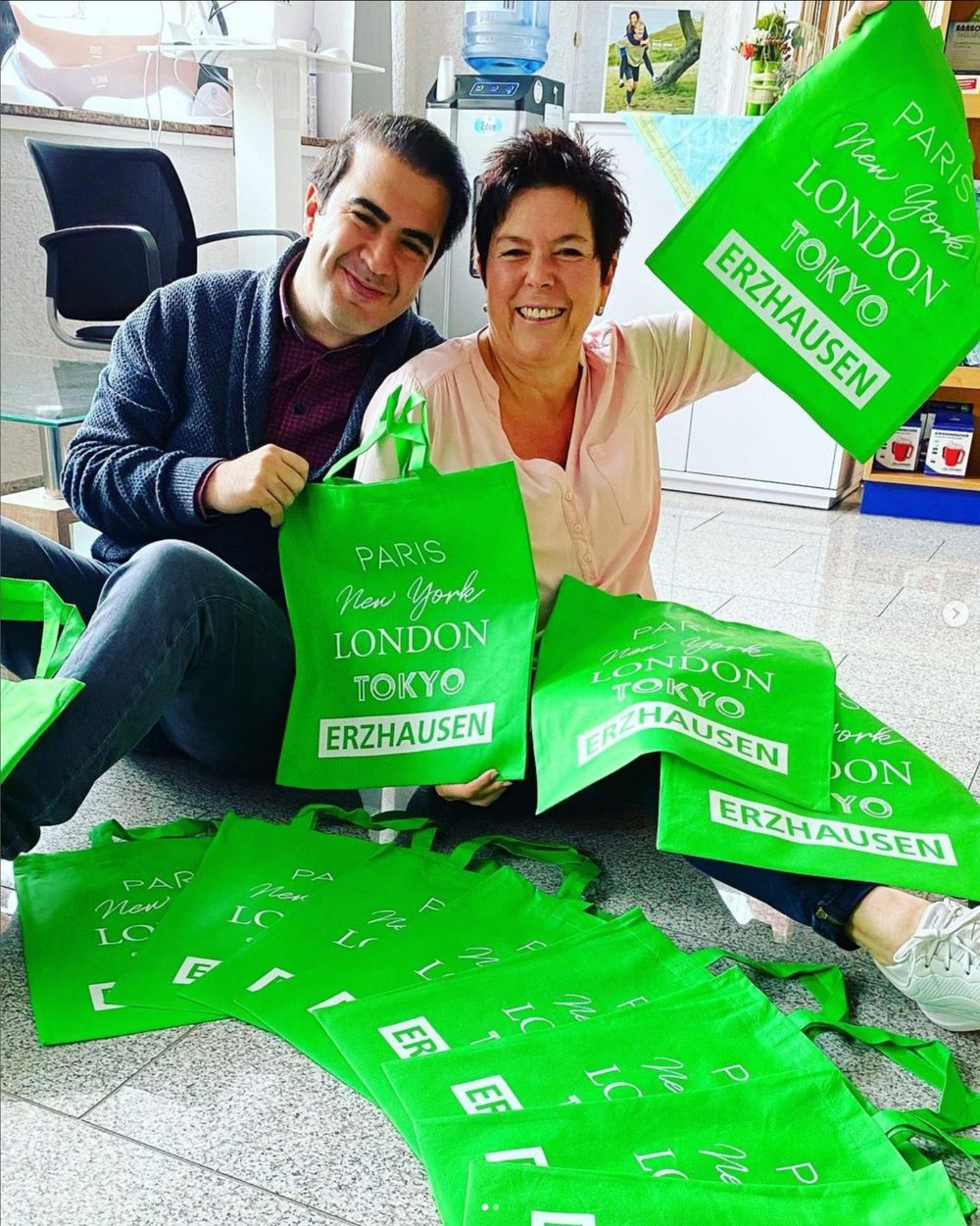 Dr. Nojan Nejatian und eine Mitarbeiterin halten grüne Stofftaschen mit dem Aufdruck Erzhausen in die Kamera
